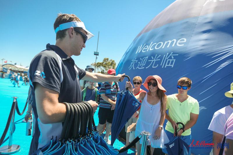 工作人員給排隊的人們分發遮陽傘（攝影 李一鳴）